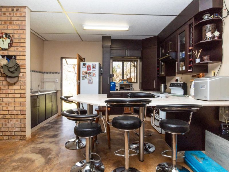 A functional kitchen featuring dark cabinetry, an exposed brick feature wall, and a breakfast bar area with direct access to the exterior.