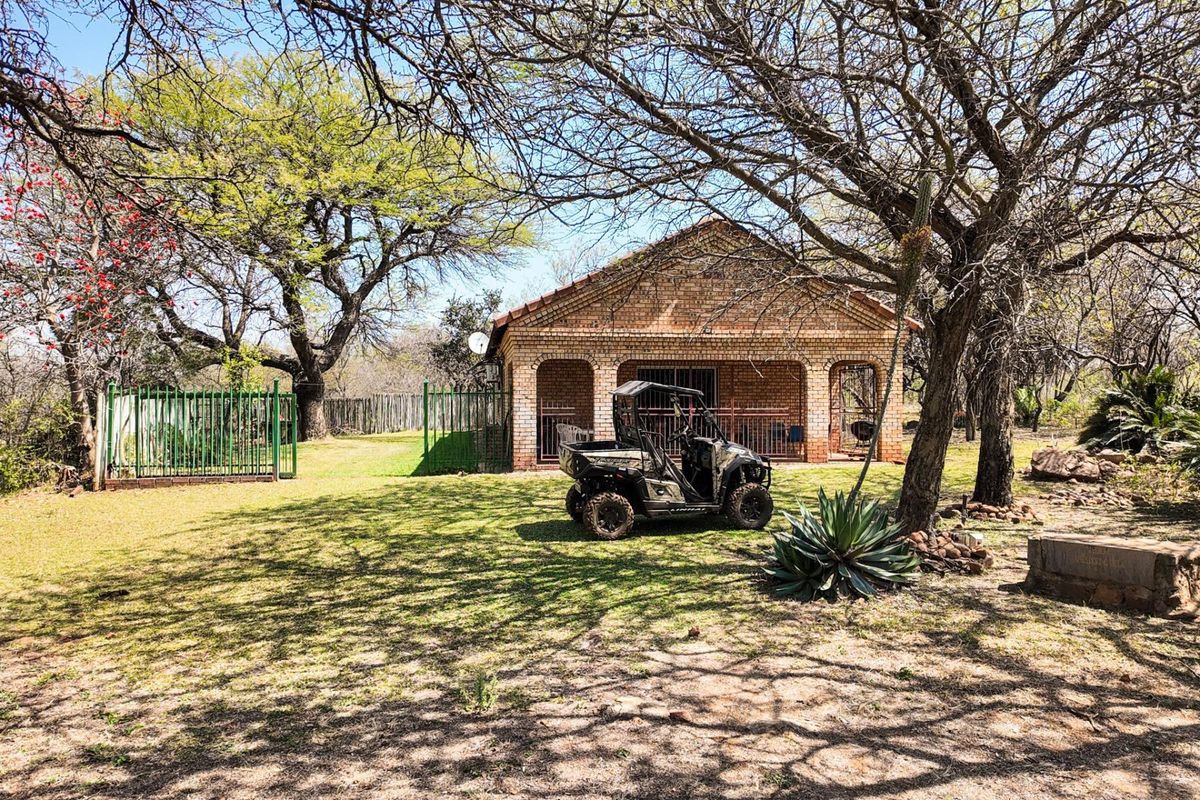 A view of the rear brick farmhouse elevation featuring an arched patio area, set within a spacious garden with mature trees and perimeter fencing.