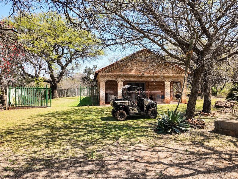 A view of the rear brick farmhouse elevation featuring an arched patio area, set within a spacious garden with mature trees and perimeter fencing.