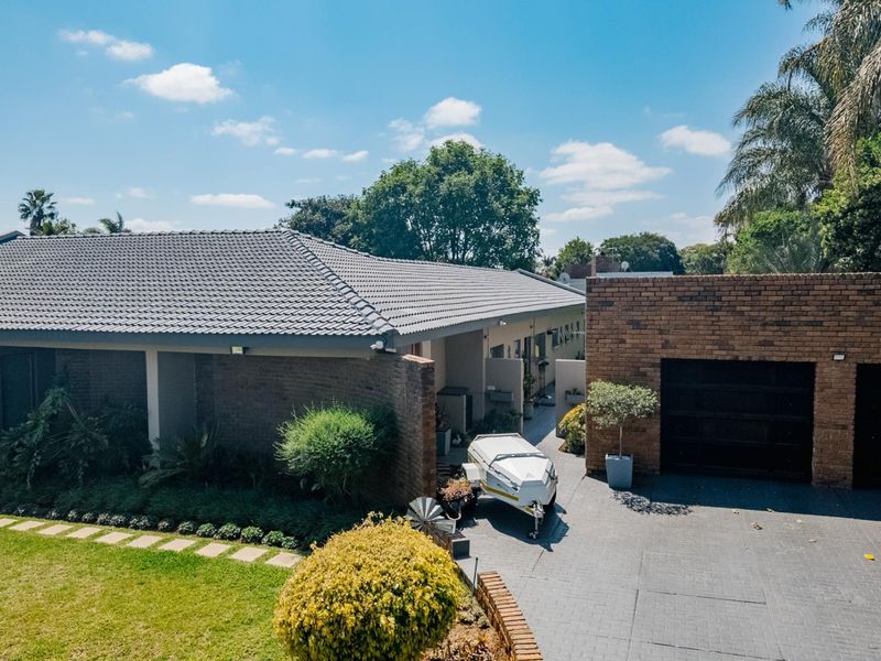 An elevated view of the front exterior featuring a brick facade, tiled roof, paved driveway, and a well-maintained garden.
