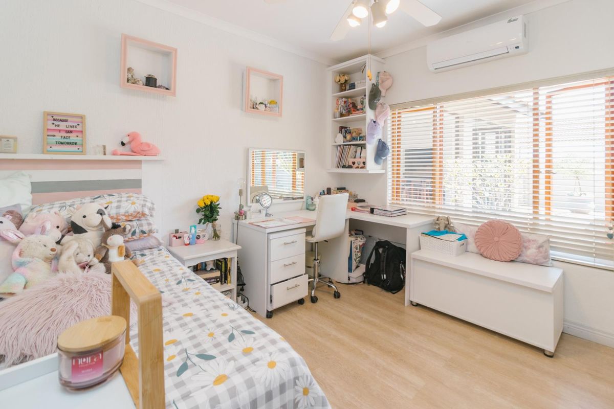 A well-maintained bedroom featuring light laminate flooring, a split-system air conditioner, built-in shelving, and a ceiling fan.