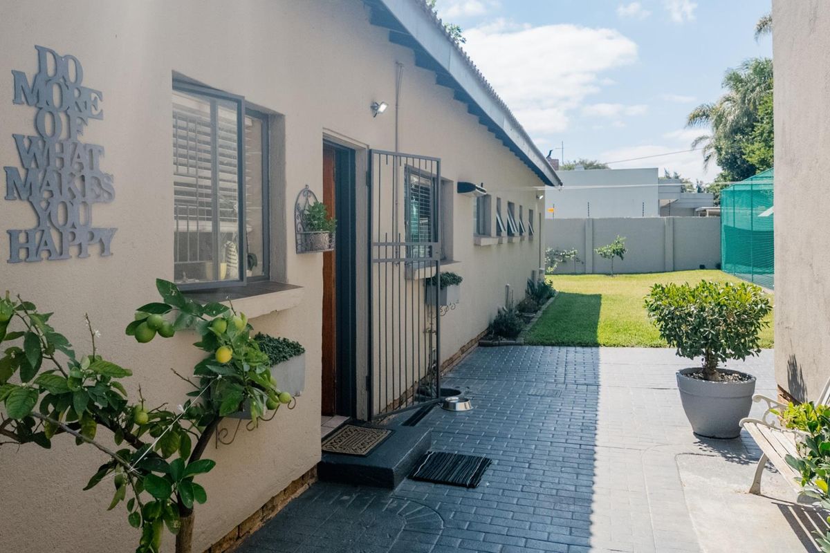 A well-maintained rear exterior view featuring a paved patio area, secure entrance gate, and a neat garden space with perimeter walling.
