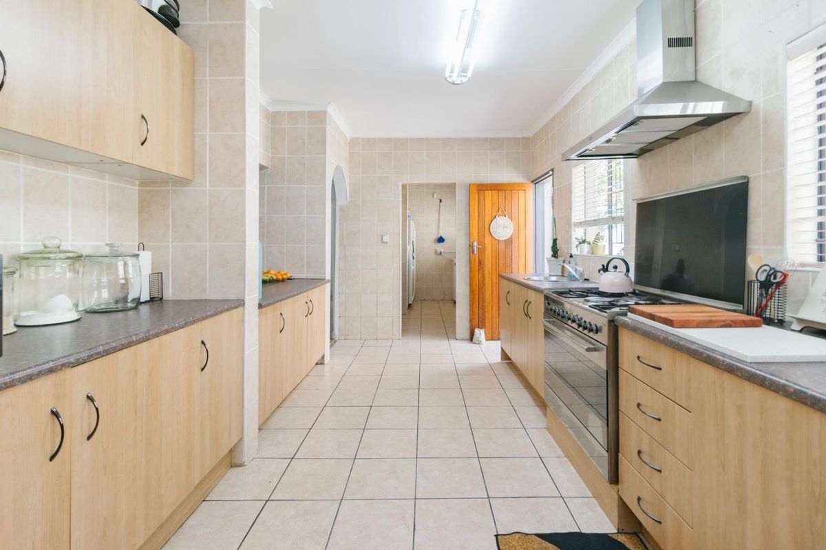 A functional kitchen featuring light wood-look cabinetry, tiled flooring, stainless steel gas stove, and an integrated extractor fan with a connected scullery area.