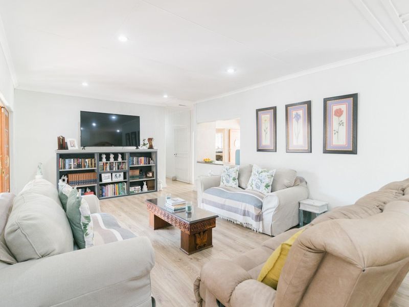 A bright and well-maintained living room featuring laminate flooring, recessed downlights, and a convenient pass-through window connecting to the kitchen area.