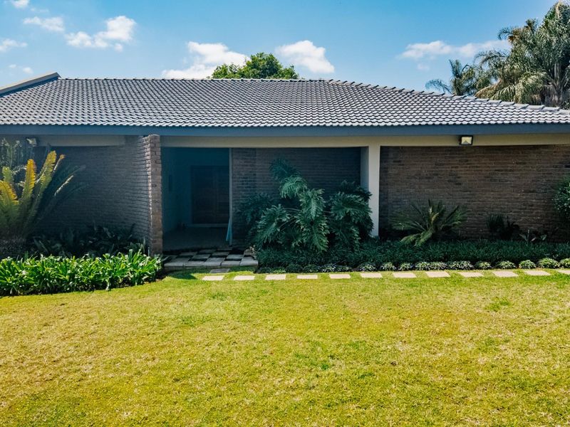 Front view of a single-story brick house featuring a tiled roof, a paved entrance walkway, and a well-maintained front garden.