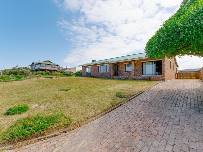 A well-maintained single-story face brick house featuring a paved driveway, metal roof, and a spacious front lawn in a coastal setting.