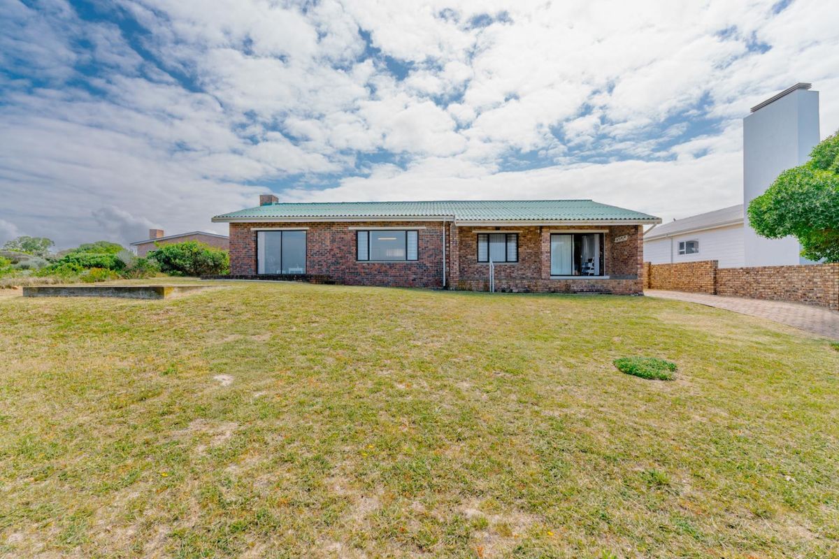 A rear view of a single-story face brick house featuring a green corrugated metal roof, large windows, and a spacious lawn area.