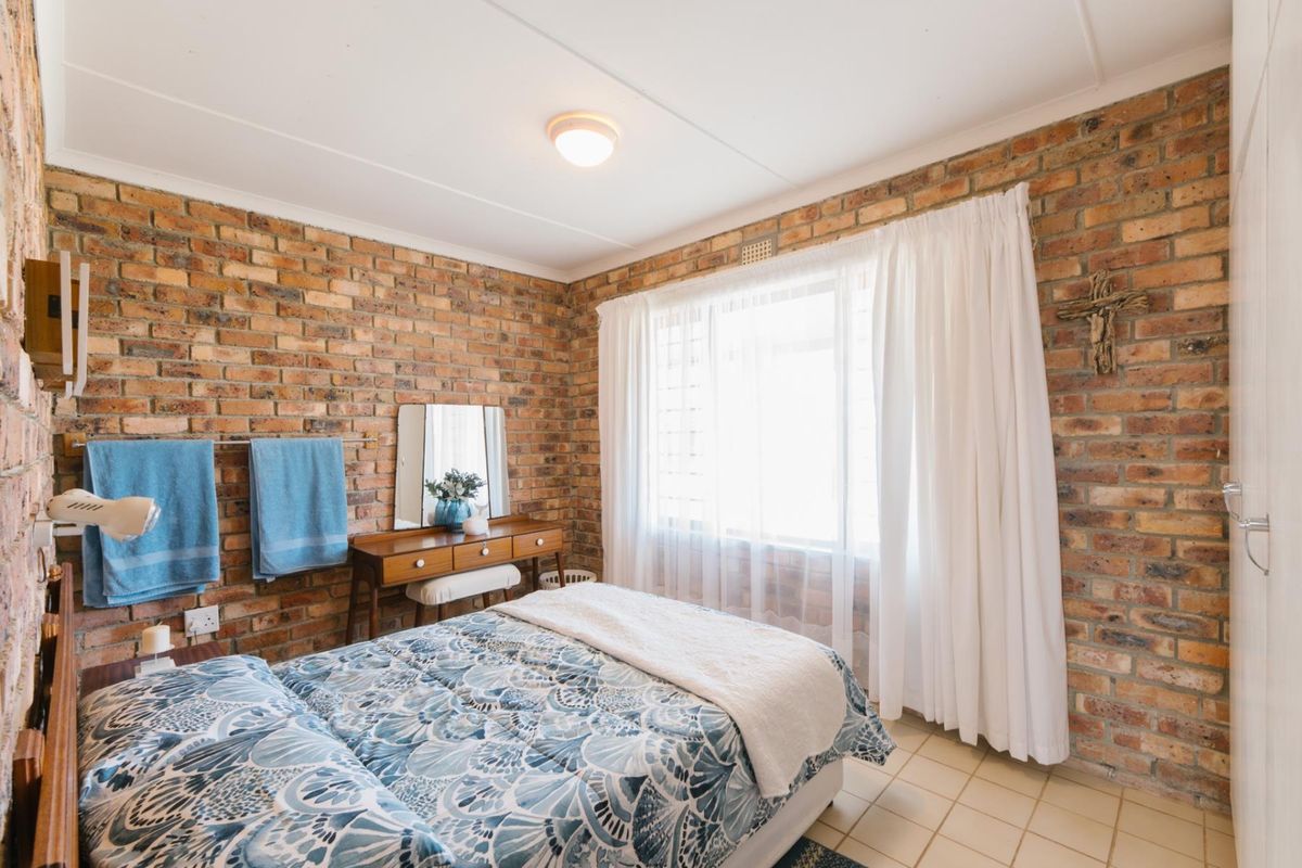 A bedroom featuring exposed brick walls, tiled flooring, and a large window allowing natural light.