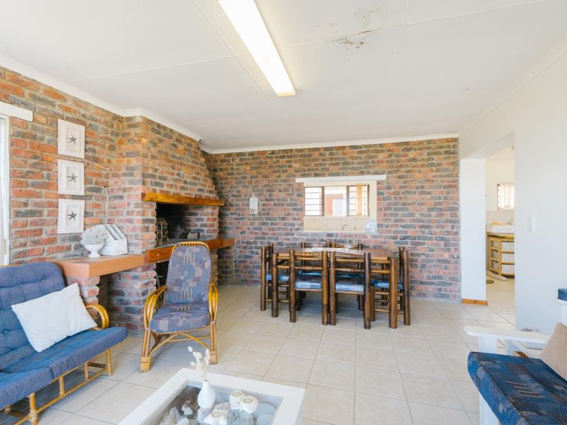 Open-plan living and dining area featuring exposed brick walls, a built-in indoor fireplace, and tiled flooring with a convenient pass-through window to the kitchen.