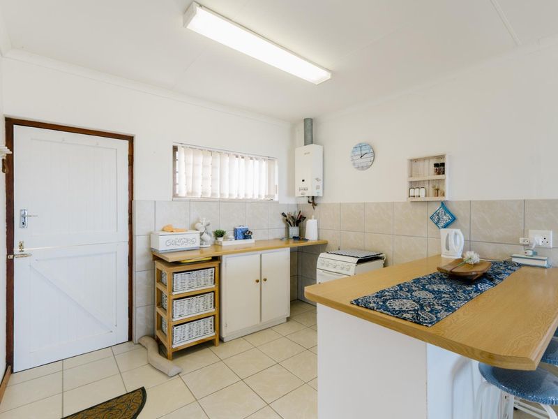 A functional kitchen featuring tiled flooring, a tiled splashback, built-in cabinetry, a gas water heater, and a breakfast bar area.