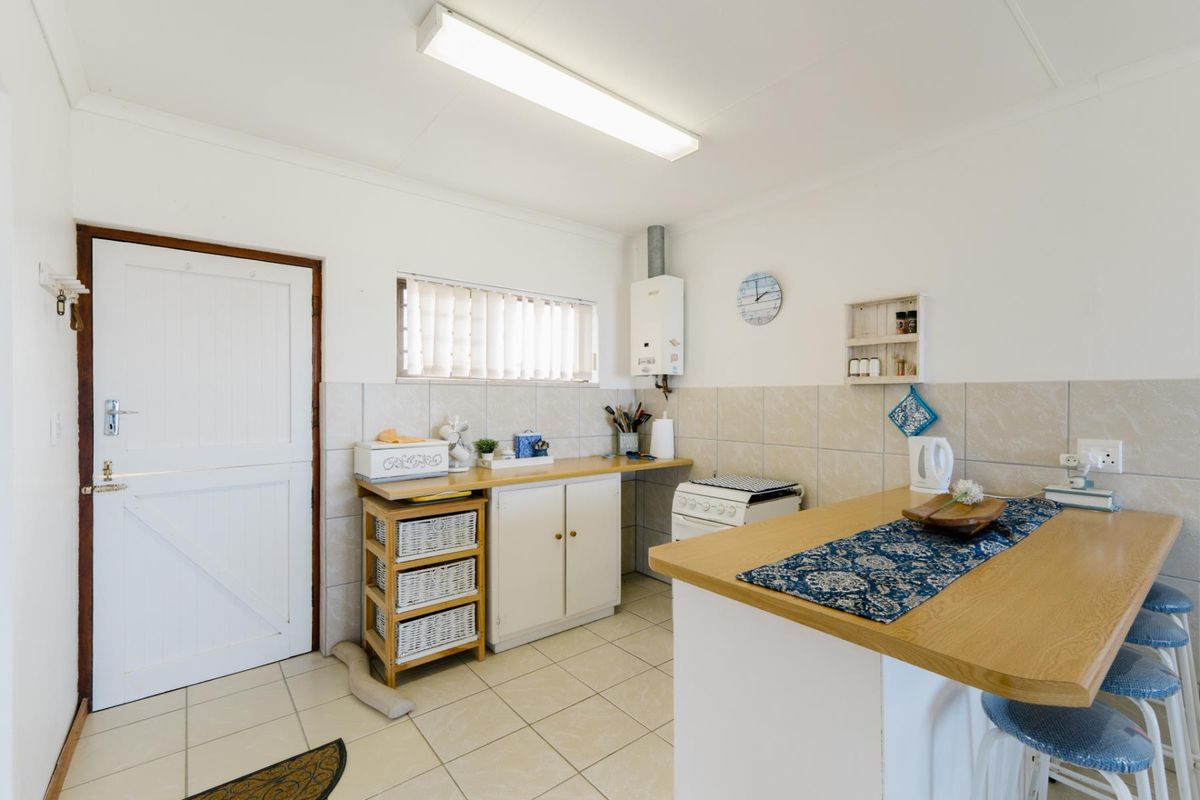 A functional kitchen featuring tiled flooring, a tiled splashback, built-in cabinetry, a gas water heater, and a breakfast bar area.