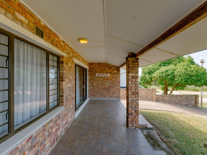 A covered outdoor patio featuring exposed brick walls, tiled flooring, and brick support columns, providing a sheltered space overlooking the front garden area.