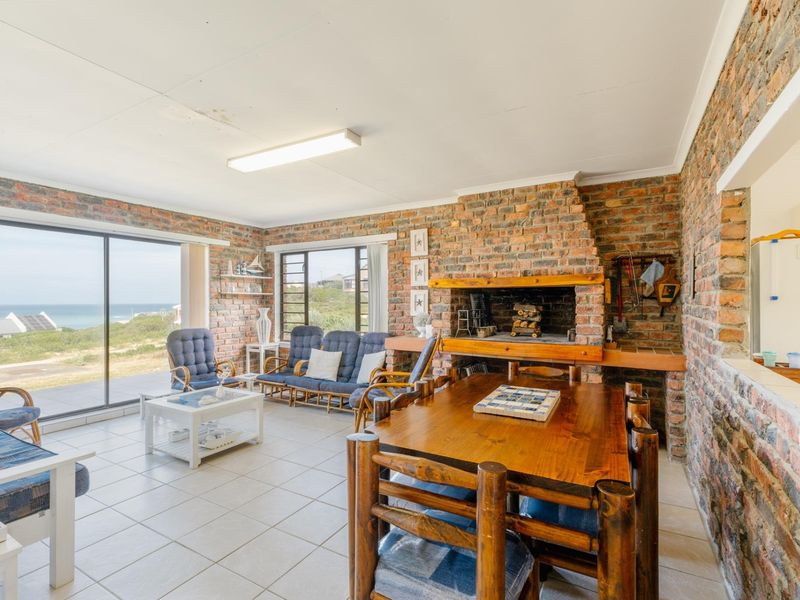 Open-plan living and dining area featuring exposed brick walls, a built-in indoor fireplace, tiled flooring, and large sliding glass doors with coastal views.