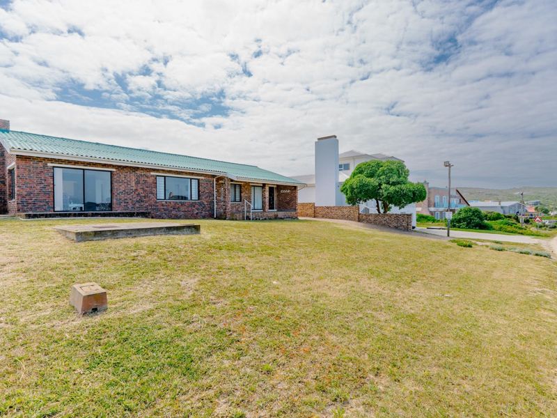 A single-story face brick house with a green metal roof, featuring large sliding doors and a spacious front lawn area.