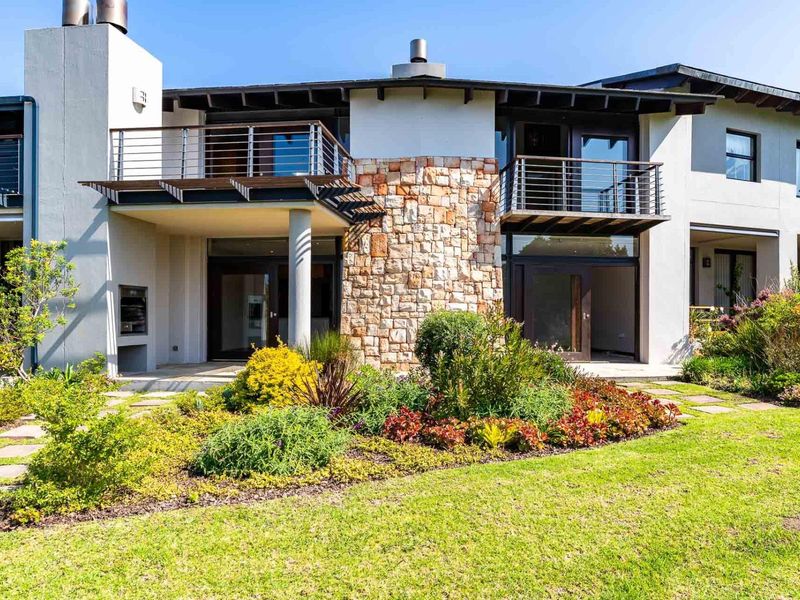 Rear elevation of the apartment featuring a landscaped garden, paved patio with built-in braai, and upper-level balconies with stainless steel balustrades.