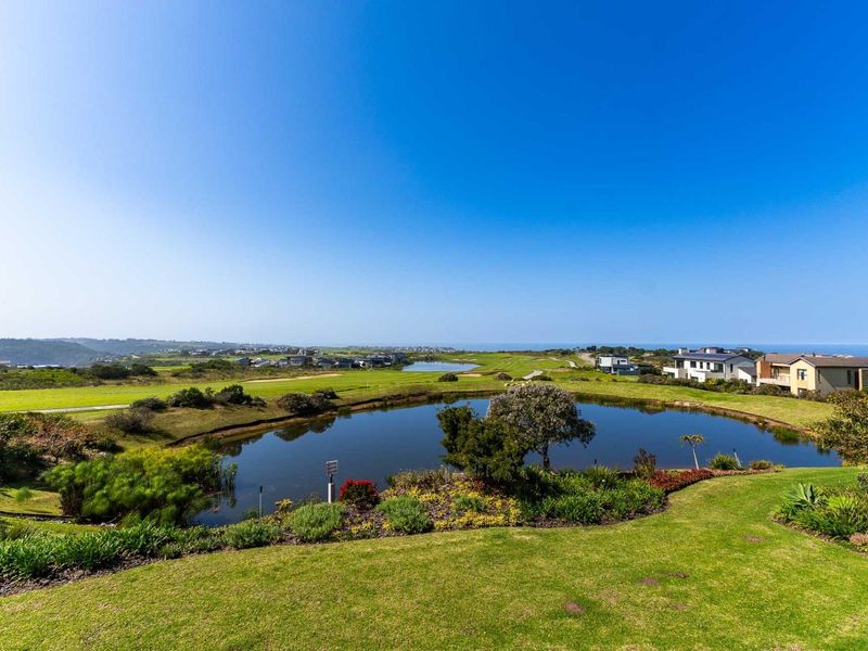 A scenic elevated view overlooking a landscaped garden, a tranquil pond, and the surrounding golf estate landscape towards the distant coastline.