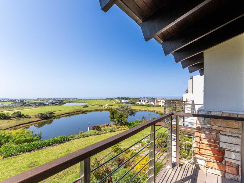 A well-maintained balcony featuring timber decking, stainless steel balustrades, and stone cladding, offering expansive views over the golf course and surrounding landscape.
