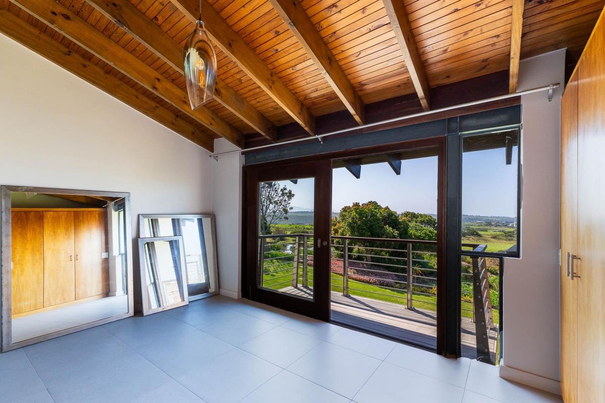 Spacious bedroom featuring exposed timber beam ceilings, tiled flooring, built-in cupboards, and sliding glass doors opening onto a balcony with scenic views.