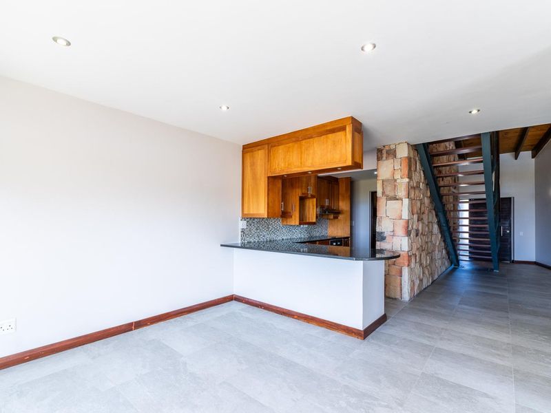 Open-plan living area featuring a kitchen with granite countertops, wooden cabinetry, a striking stone feature wall, and an open-tread staircase.