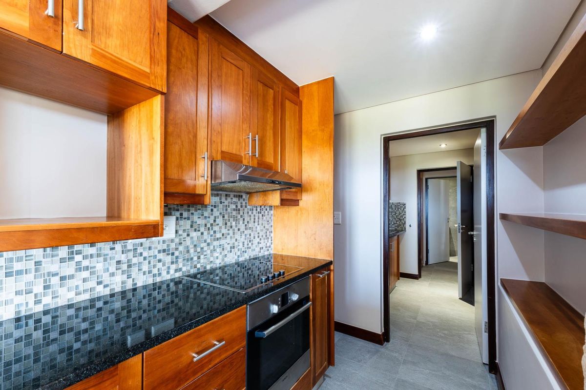A modern kitchen featuring warm wooden cabinetry, granite countertops, a mosaic tile backsplash, and integrated stainless steel appliances with tiled flooring.