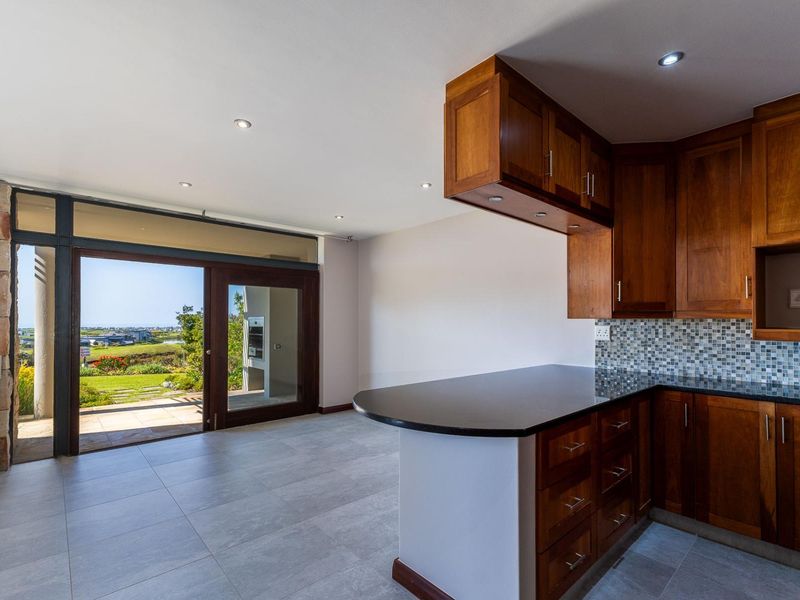 Open-plan kitchen and living area featuring warm wooden cabinetry, granite countertops, mosaic backsplash, and large sliding doors leading to an outdoor patio.