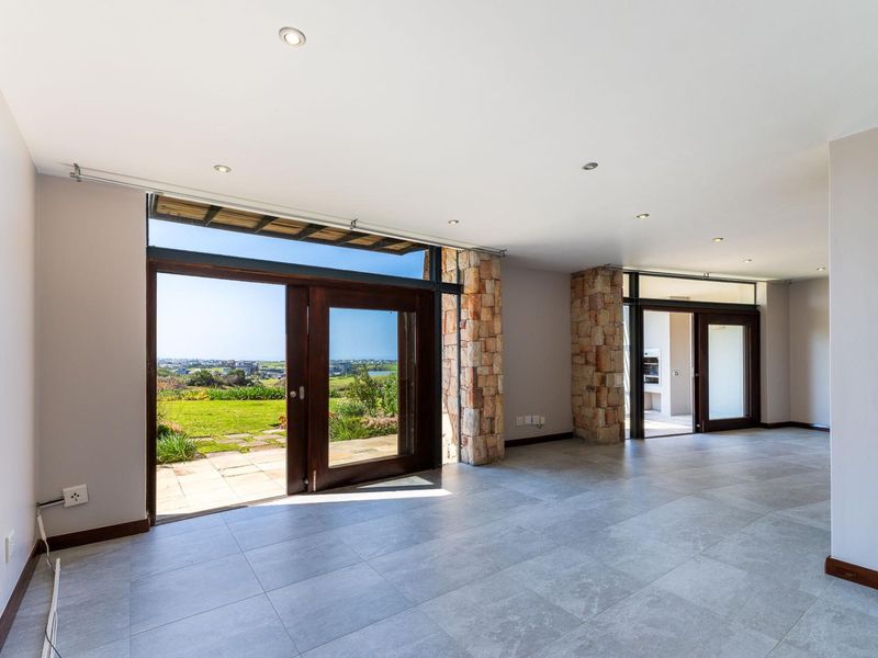 Spacious, light-filled living area featuring large timber-framed sliding doors, stone-clad pillars, and modern tiled flooring, offering seamless access to the outdoor patio and garden.