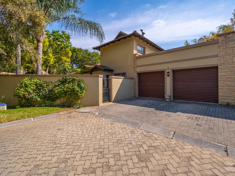 Front elevation of the property featuring a double garage, paved driveway, and secure boundary wall with pedestrian access.