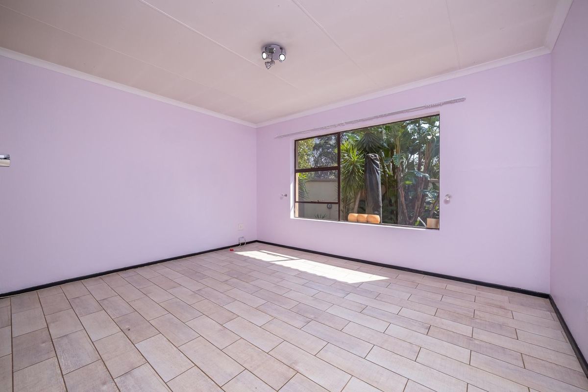 A bright, empty bedroom featuring light-toned tiled flooring, neutral walls, and a large window overlooking the garden.