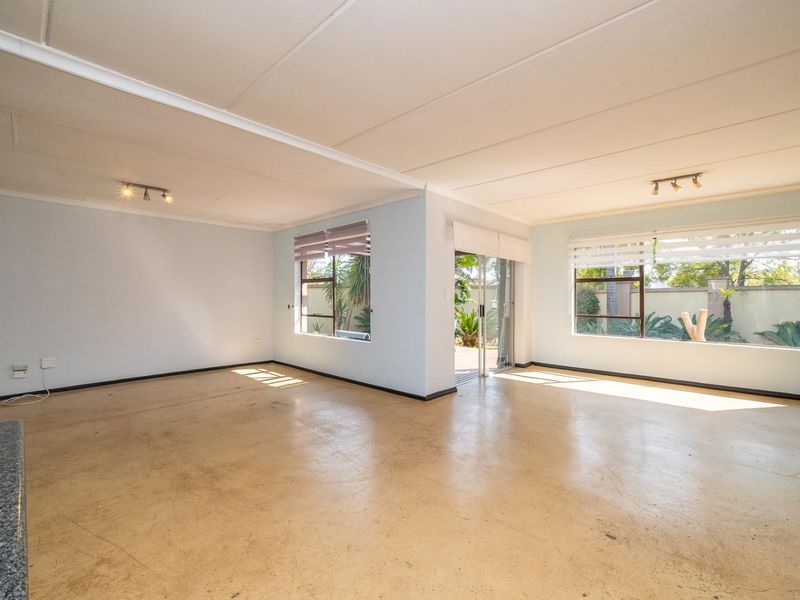 Spacious open-plan living area featuring large windows, track lighting, and direct access to the outdoor patio through a sliding glass door.