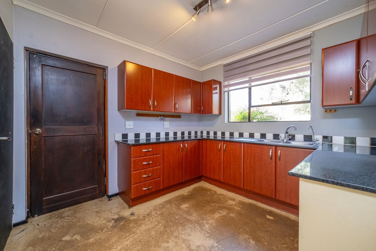 A functional kitchen featuring wood-look cabinetry, granite countertops, and a tiled splashback, currently awaiting new flooring to complete the space.