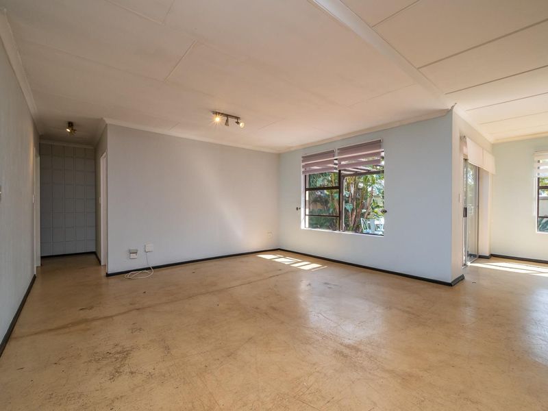 An empty, open-plan living area featuring tiled flooring, large windows with blinds, and sliding door access to the garden.