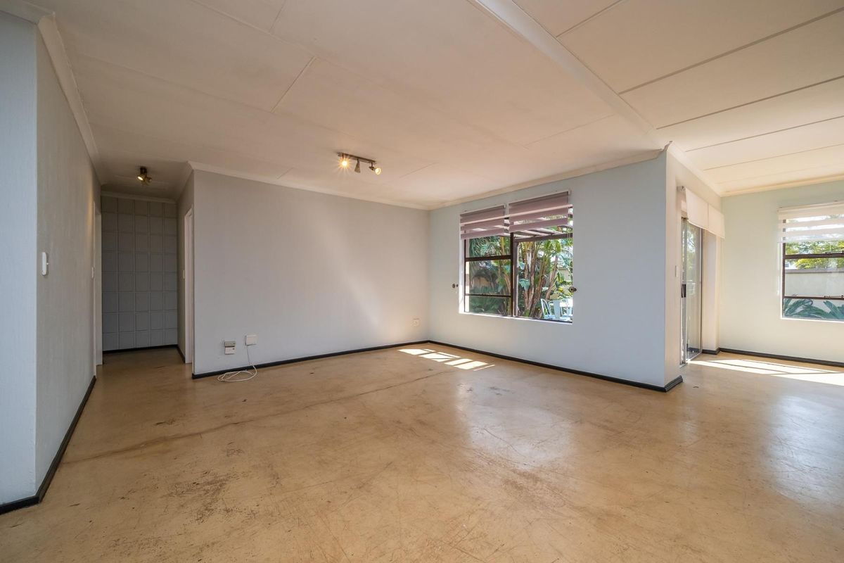 An empty, open-plan living area featuring tiled flooring, large windows with blinds, and sliding door access to the garden.