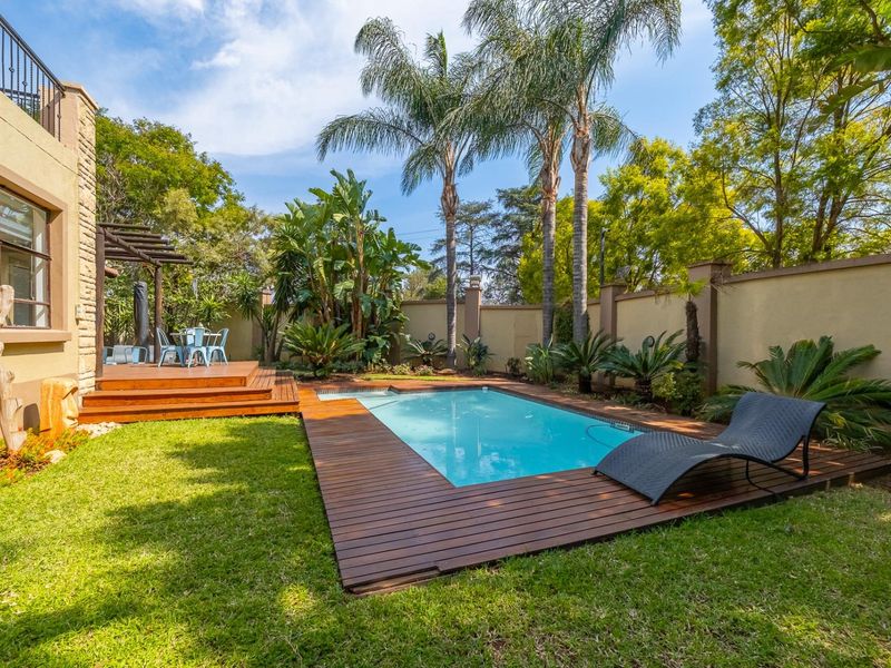 A well-maintained backyard featuring a swimming pool with timber decking, a pergola-covered patio area, and established garden landscaping.
