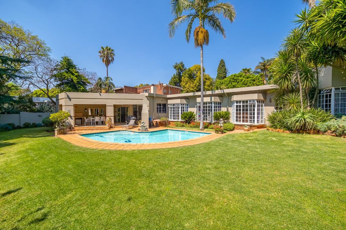 Rear view of the property featuring a swimming pool, covered patio area, and well-maintained garden with mature trees.