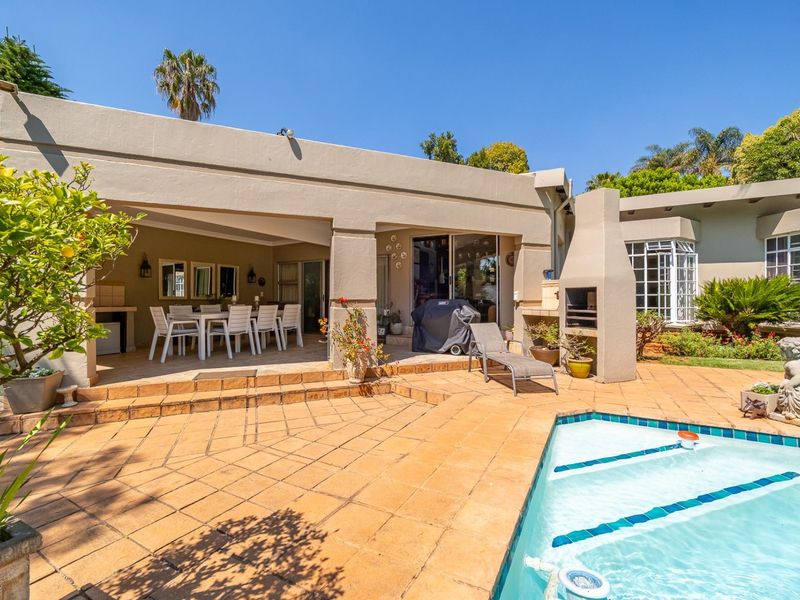 Covered outdoor patio area featuring a built-in braai, overlooking a swimming pool with tiled surround and direct access to the main living area.