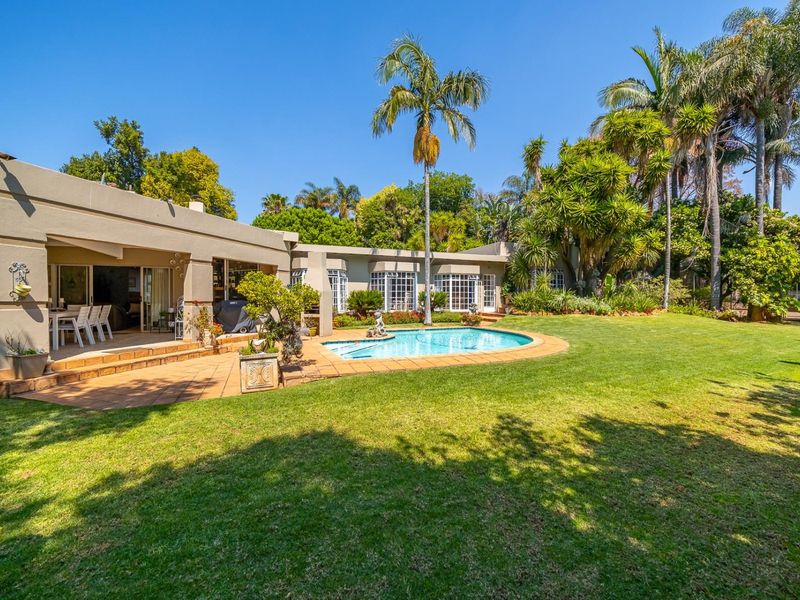 Spacious rear exterior featuring a well-maintained swimming pool, paved patio area, and lush landscaped garden with mature palm trees.