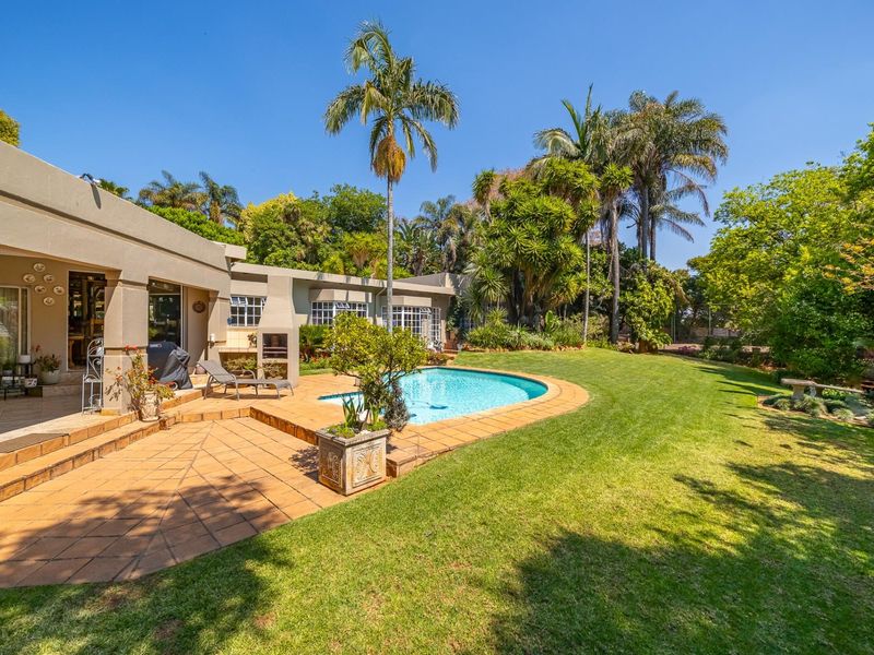 Spacious outdoor entertainment area featuring a swimming pool, tiled patio, built-in braai, and a well-maintained landscaped garden.