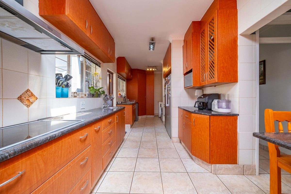 A functional kitchen featuring warm-toned wooden cabinetry, granite countertops, tiled flooring, and a built-in hob with an extractor fan.