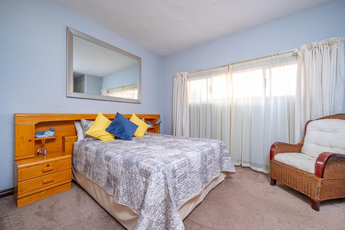 A bedroom featuring a built-in wooden headboard with integrated bedside tables, carpeted flooring, and large windows with curtains.