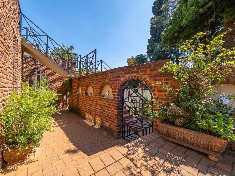 A charming rear exterior area featuring exposed brick walls, a paved patio, and a metal staircase leading to an upper level.