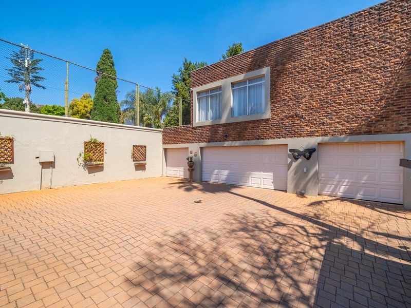 A well-maintained exterior view featuring a paved driveway, triple garage doors, and a distinctive brick facade with perimeter fencing.