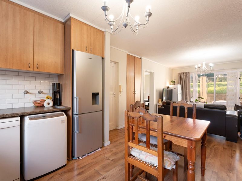 Open-plan kitchen and dining area featuring laminate flooring, subway tile backsplash, and built-in cabinetry, leading to a bright living space with sliding door access.