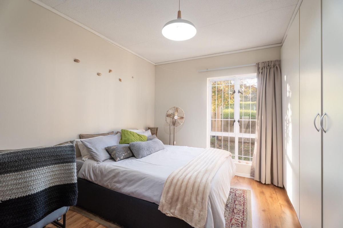 A well-lit bedroom featuring laminate flooring, built-in cupboards, and a secure window with access to the exterior.