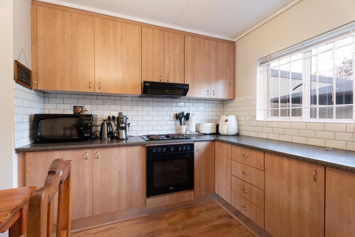 Functional kitchen featuring light wood-tone cabinetry, subway tile backsplash, dark laminate countertops, and integrated cooking appliances with a window for natural light.