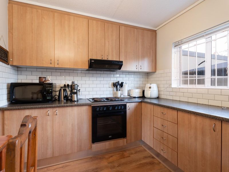 Functional kitchen featuring light wood-tone cabinetry, subway tile backsplash, dark laminate countertops, and integrated cooking appliances with a window for natural light.