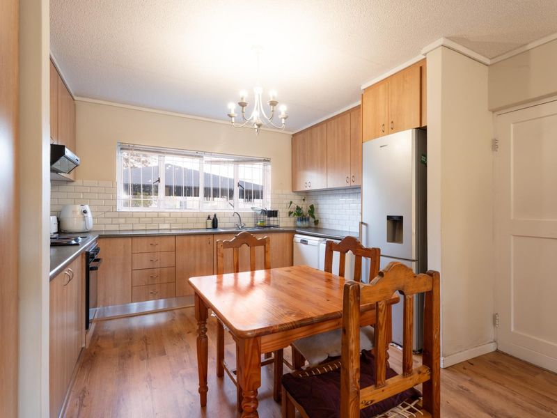A functional kitchen featuring light wood cabinetry, subway tile backsplash, laminate countertops, and integrated appliances, with an adjacent dining area.