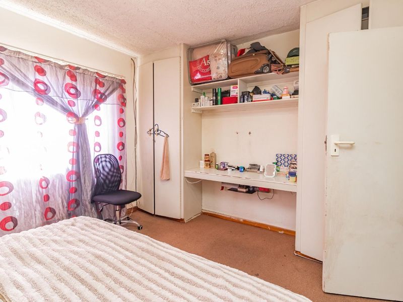 Bedroom featuring built-in wardrobe, desk, and shelving units. The room includes carpeted flooring and a window with natural light.