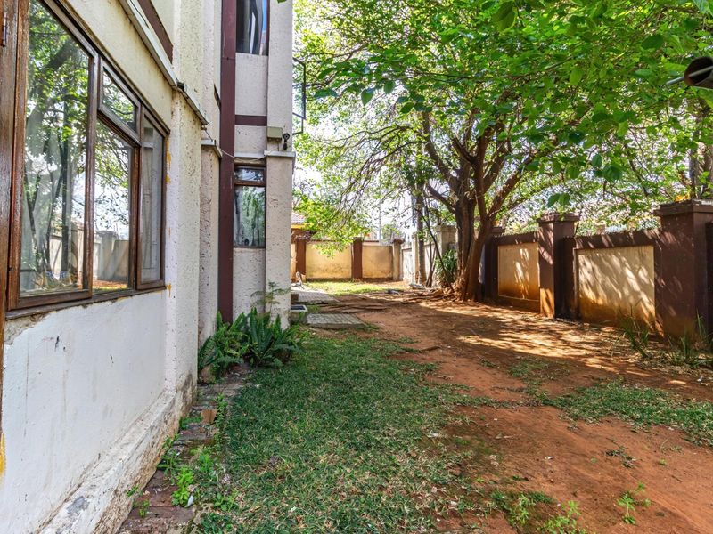 A view of the rear exterior area featuring a perimeter boundary wall, mature trees, and a side facade with timber-framed windows.