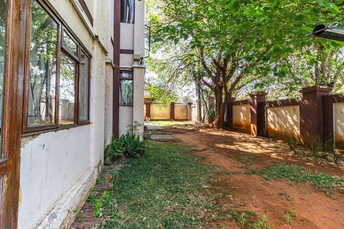 A view of the rear exterior area featuring a perimeter boundary wall, mature trees, and a side facade with timber-framed windows.