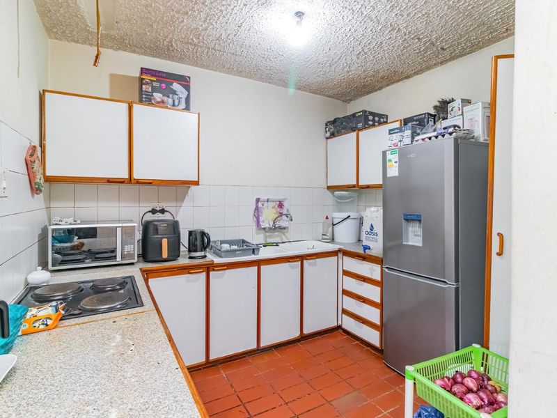A functional kitchen featuring built-in cabinetry, laminate countertops, an electric hob, and a double basin sink with tiled backsplash and flooring.